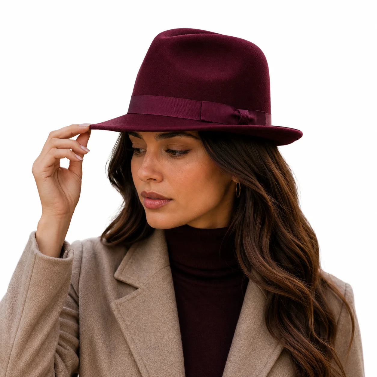 Woman wearing a burgundy fedora hat with a beige coat on a white background