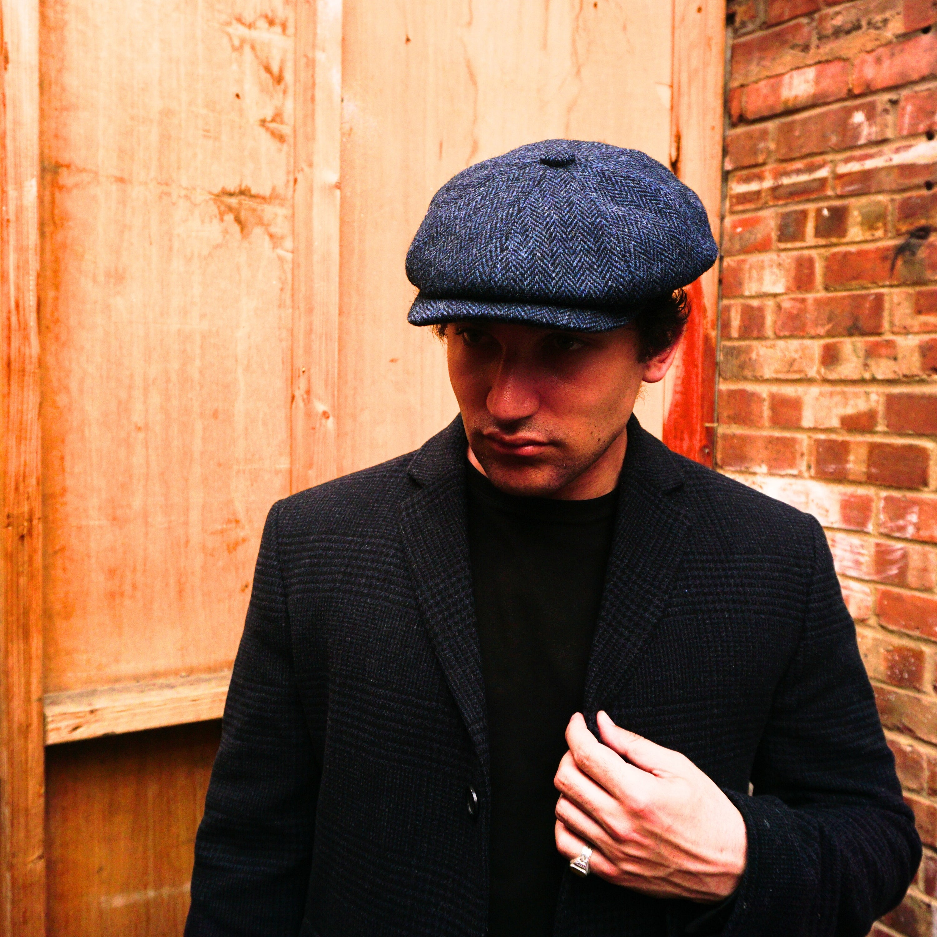 Navy Harris Tweed Herringbone Newsboy Cap, crafted from 100% pure new wool, handwoven in Scotland’s Outer Hebrides. Features include a sewn-down brim, cotton lining, and a removable Gladwin Bond side pin. Available in sizes S-XL. Inspired by the iconic Peaky Blinders style.